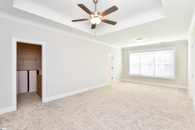 empty room with a ceiling fan, crown molding, baseboards, a tray ceiling, and carpet flooring