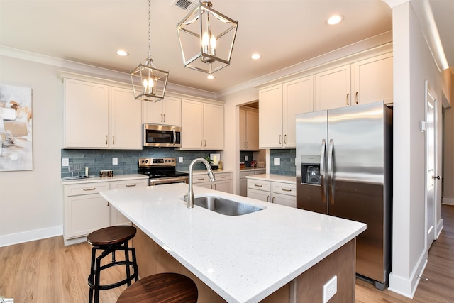kitchen featuring a kitchen island with sink, baseboards, light wood-type flooring, a sink, and stainless steel appliances
