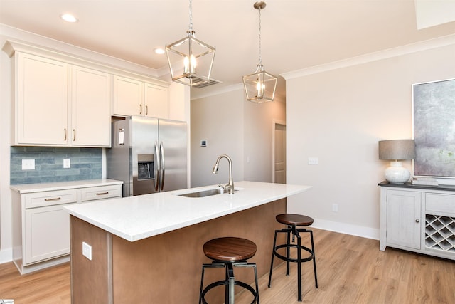 kitchen featuring ornamental molding, a breakfast bar area, stainless steel refrigerator with ice dispenser, light wood-type flooring, and a sink