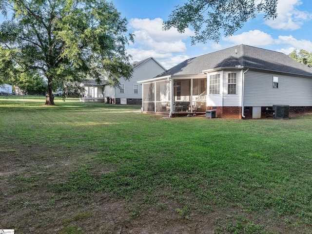 rear view of house featuring a sunroom, roof with shingles, central air condition unit, and a yard