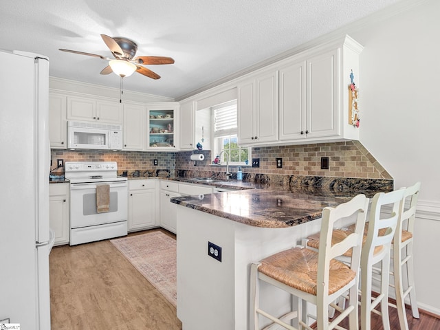 kitchen with a sink, light wood-style floors, a peninsula, and white appliances