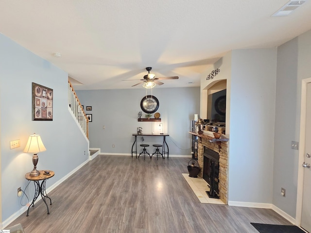 living room with a ceiling fan, visible vents, wood finished floors, and a fireplace