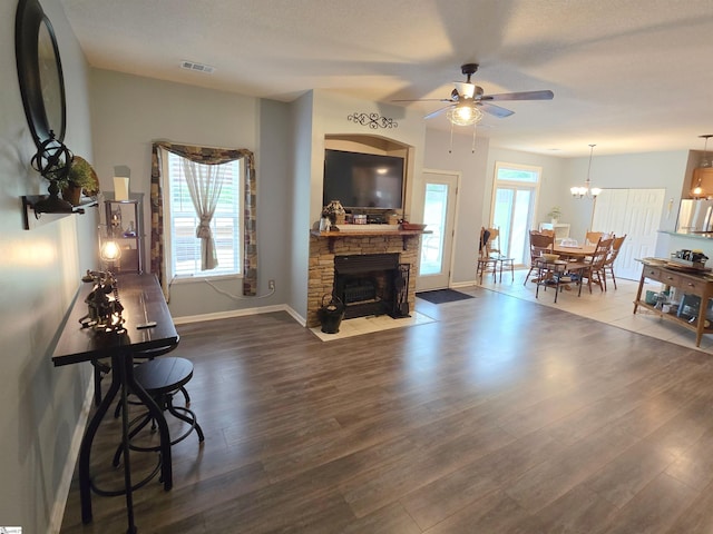 living area with ceiling fan, visible vents, a fireplace, wood finished floors, and baseboards