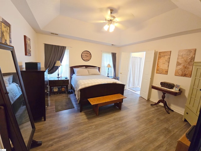 bedroom featuring dark wood-style flooring, a ceiling fan, baseboards, a tray ceiling, and visible vents