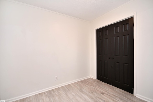 unfurnished bedroom featuring light wood-style floors, baseboards, crown molding, and a closet