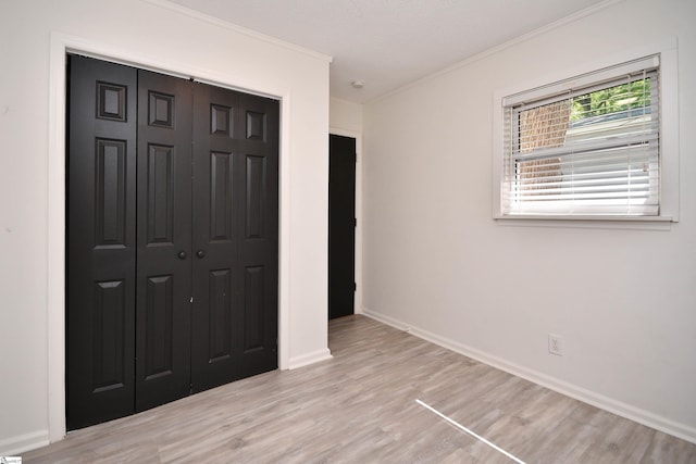 unfurnished bedroom with light wood-style floors, baseboards, ornamental molding, and a closet