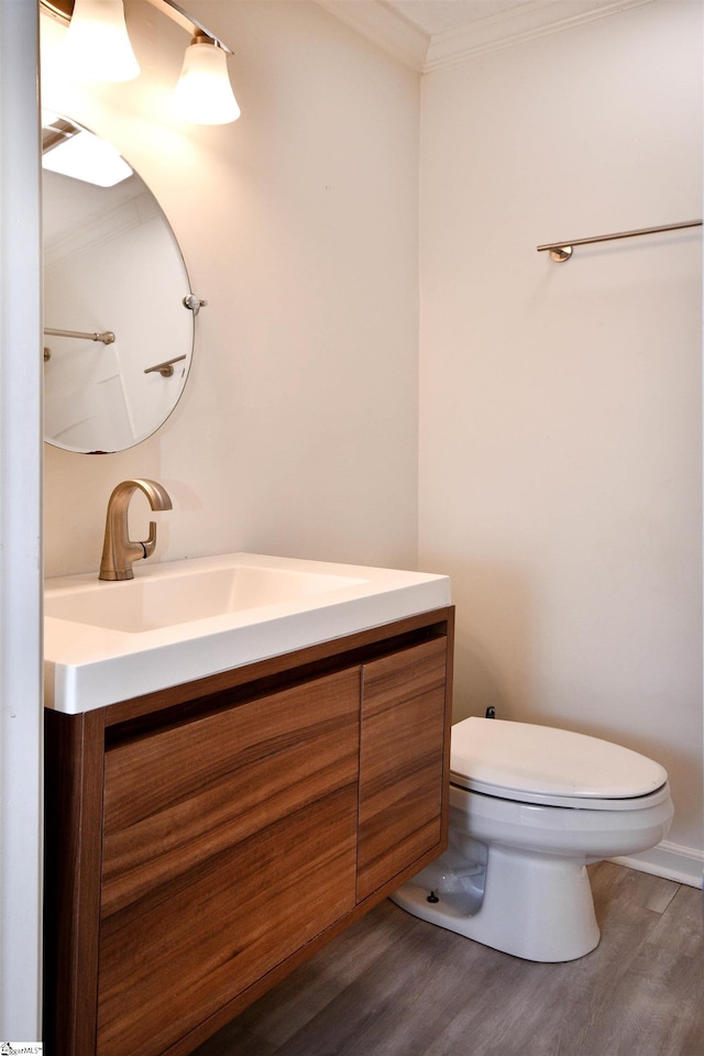 half bathroom with vanity, ornamental molding, wood finished floors, and toilet