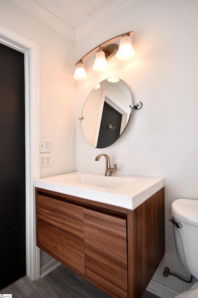 half bath with toilet, ornamental molding, wood finished floors, and vanity