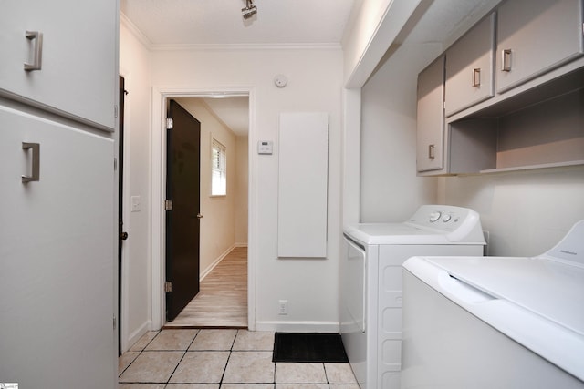 clothes washing area with ornamental molding, light tile patterned flooring, baseboards, separate washer and dryer, and cabinet space