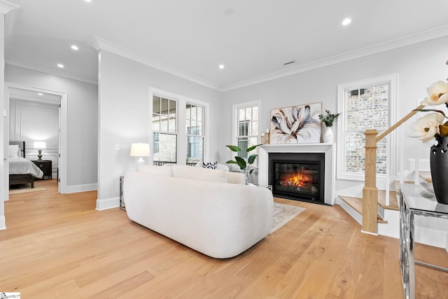 living room with crown molding, recessed lighting, a fireplace with flush hearth, and light wood-style floors
