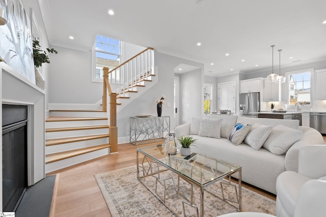 living room with stairs, recessed lighting, crown molding, and light wood-style floors