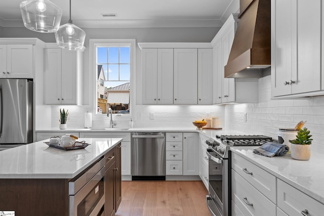 kitchen featuring visible vents, appliances with stainless steel finishes, a sink, custom exhaust hood, and light wood-style flooring