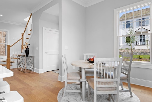 dining room featuring light wood-style floors, ornamental molding, stairs, and baseboards