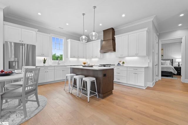 kitchen with stainless steel refrigerator with ice dispenser, ornamental molding, a kitchen island, and premium range hood