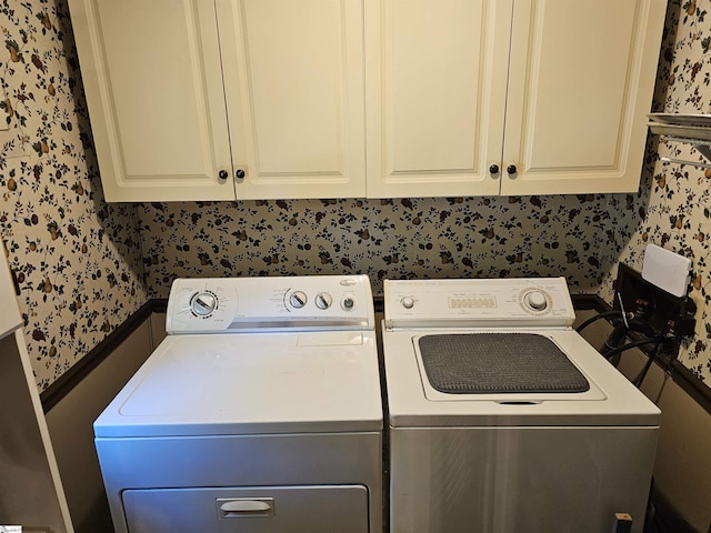 clothes washing area with cabinet space, washing machine and clothes dryer, and wallpapered walls