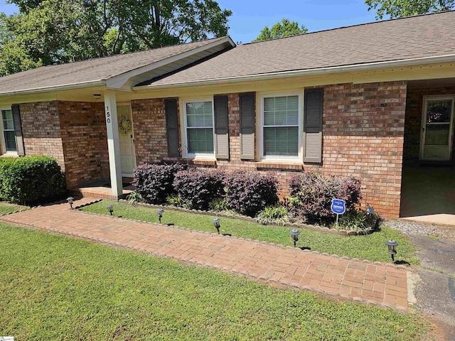 exterior space with roof with shingles, a front yard, and brick siding