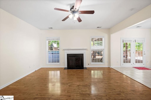 unfurnished living room featuring ceiling fan, a fireplace with flush hearth, wood finished floors, and visible vents