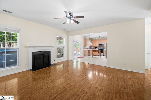 unfurnished living room with visible vents, baseboards, rail lighting, a ceiling fan, and light wood-style flooring