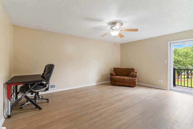 home office with light wood-style floors, a textured ceiling, a ceiling fan, baseboards, and visible vents