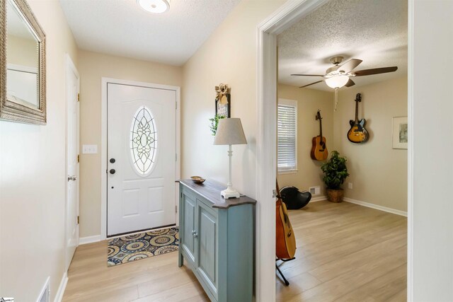 foyer entrance featuring light wood-style floors, a textured ceiling, ceiling fan, and a healthy amount of sunlight