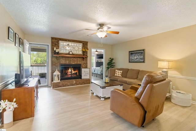 living area with light wood-type flooring, a textured ceiling, ceiling fan, and a fireplace