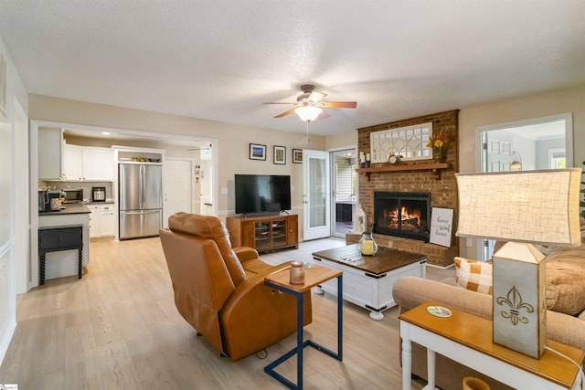 living area with light wood-style floors, a ceiling fan, and a brick fireplace