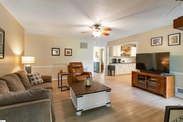 living room with light wood-style floors, ceiling fan, a textured ceiling, and visible vents