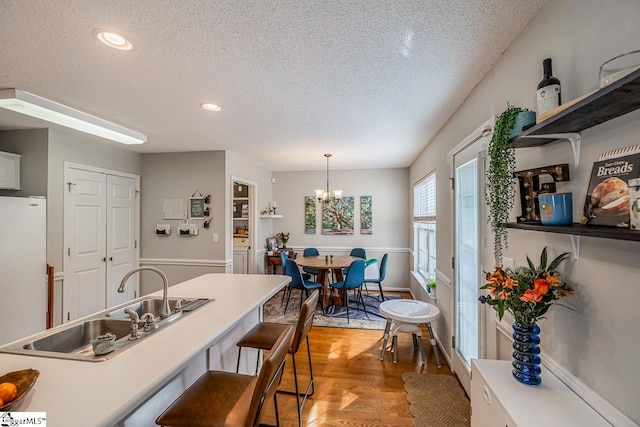 kitchen with open shelves, freestanding refrigerator, a textured ceiling, a sink, and light wood-style flooring