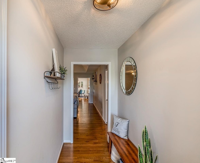 hallway with baseboards, a textured ceiling, and wood finished floors