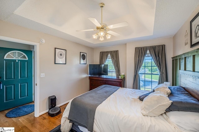 bedroom featuring a raised ceiling, baseboards, a ceiling fan, and wood finished floors