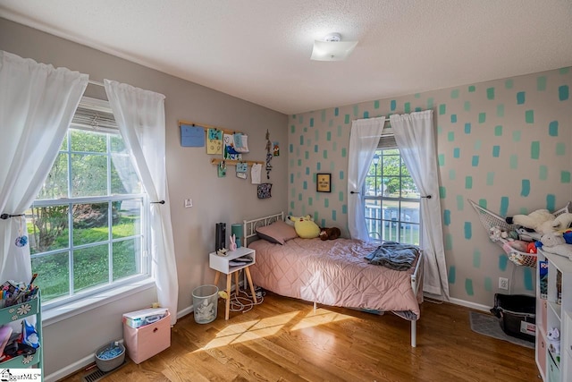 bedroom featuring baseboards, a textured ceiling, wallpapered walls, and wood finished floors