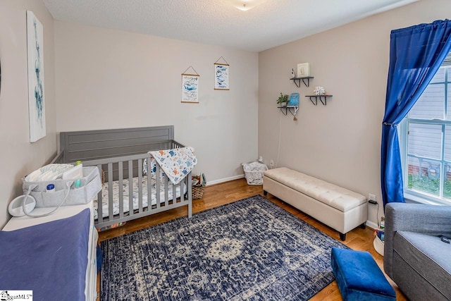 bedroom with baseboards, wood finished floors, and a nursery area