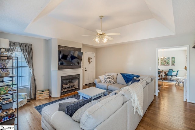 living area featuring ceiling fan with notable chandelier, wood finished floors, a tray ceiling, and a fireplace