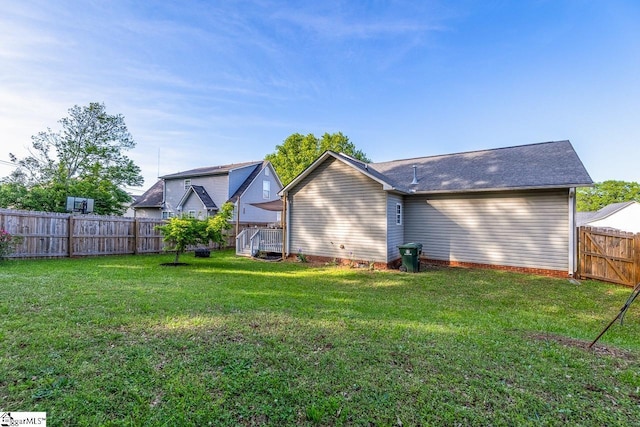 rear view of house with a fenced backyard, roof with shingles, and a yard