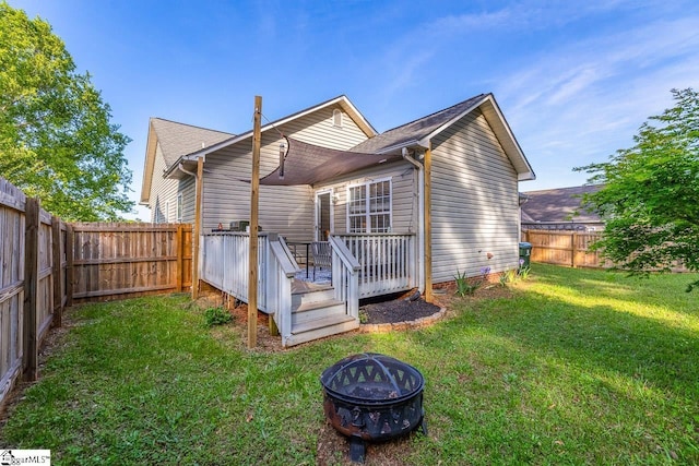 back of house with a fenced backyard, a wooden deck, a yard, and a fire pit