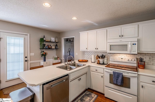 kitchen featuring a sink, white appliances, light countertops, a peninsula, and tasteful backsplash