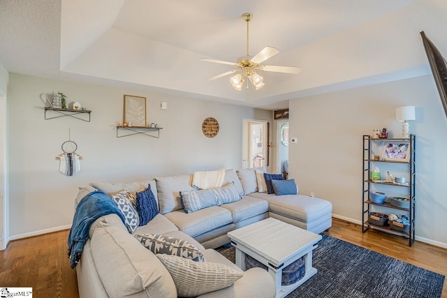 living area featuring baseboards, a ceiling fan, wood finished floors, and a tray ceiling