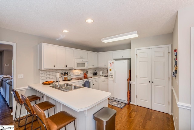 kitchen with a sink, white appliances, a peninsula, wood finished floors, and tasteful backsplash