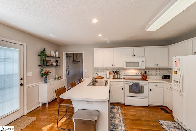 kitchen with white appliances, a peninsula, decorative backsplash, and a sink