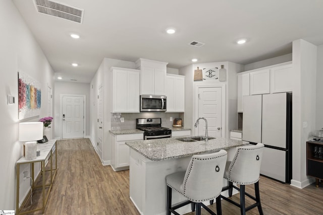 kitchen featuring light stone countertops, appliances with stainless steel finishes, a sink, wood finished floors, and visible vents