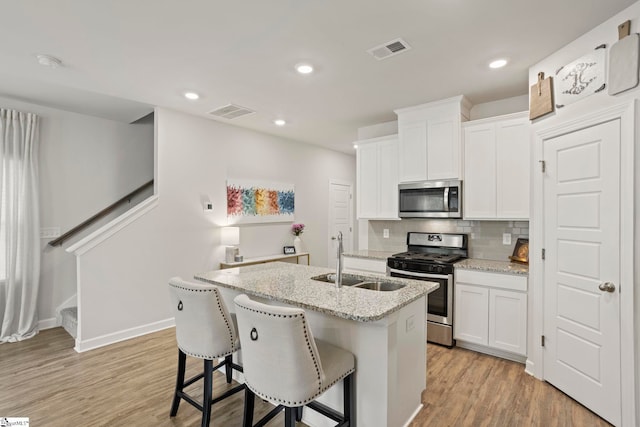 kitchen with backsplash, visible vents, appliances with stainless steel finishes, a sink, and light wood-style flooring