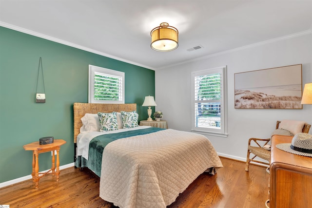 bedroom with ornamental molding, multiple windows, wood finished floors, and visible vents