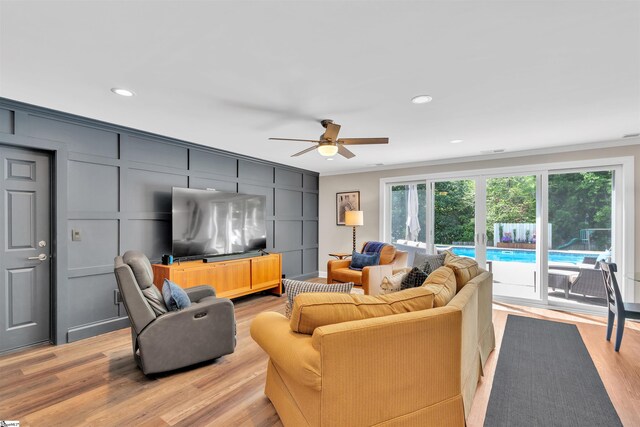living area with ornamental molding, light wood finished floors, ceiling fan, and a decorative wall
