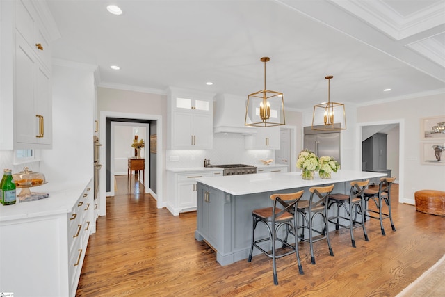 kitchen with a breakfast bar, built in refrigerator, white cabinetry, custom range hood, and backsplash
