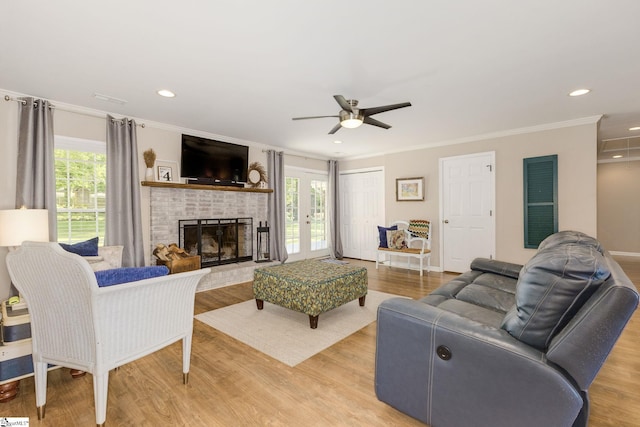 living room with crown molding, a brick fireplace, ceiling fan, recessed lighting, and light wood finished floors