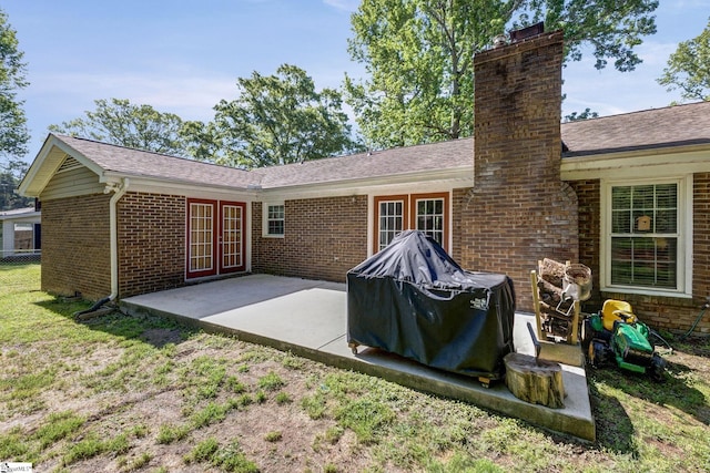 back of property featuring brick siding, french doors, a patio, and a chimney