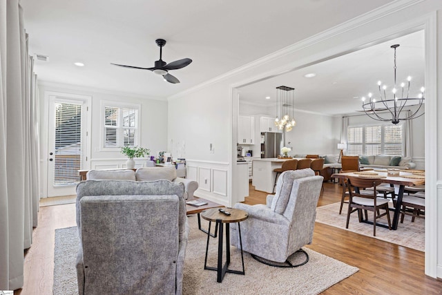 living room with a decorative wall, light wood-style flooring, ceiling fan with notable chandelier, visible vents, and ornamental molding
