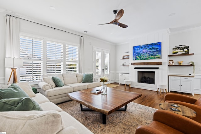 living room with crown molding, a fireplace, a decorative wall, a ceiling fan, and wood finished floors