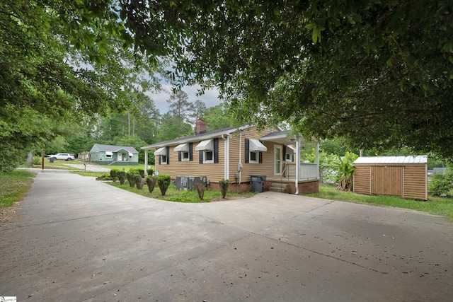 view of front facade featuring concrete driveway, an outdoor structure, a chimney, and a shed