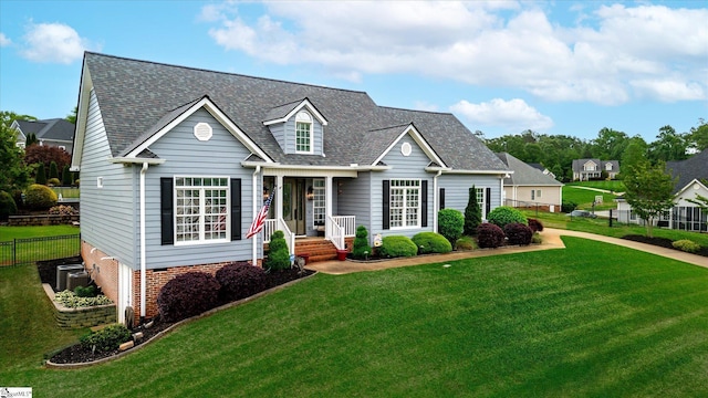 cape cod home with fence, central air condition unit, roof with shingles, and a front yard